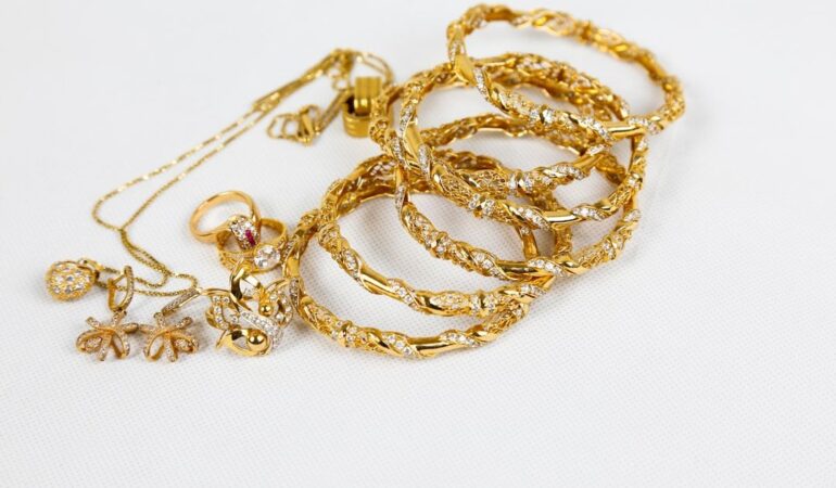 Exklusiva guldsmycken med armband, ringar och halsband på vit bakgrund.