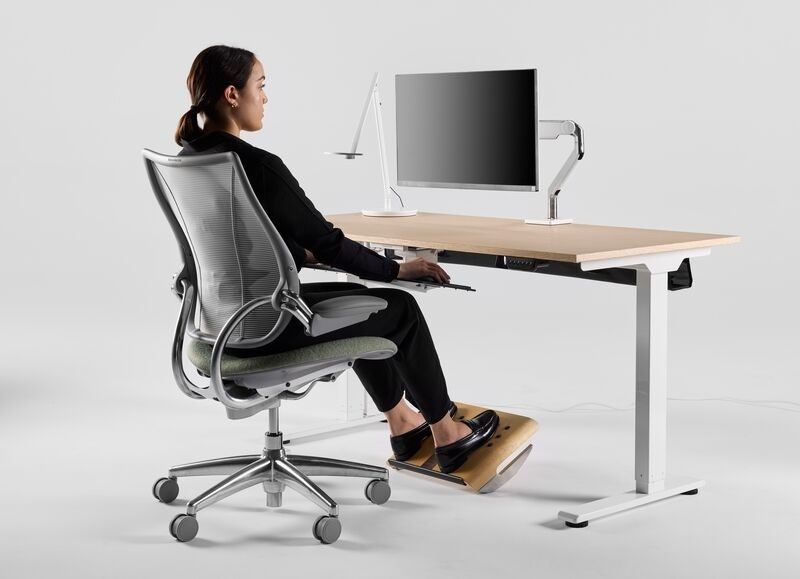 Person arbetar vid kompakt skrivbord med skärm och ergonomisk stol