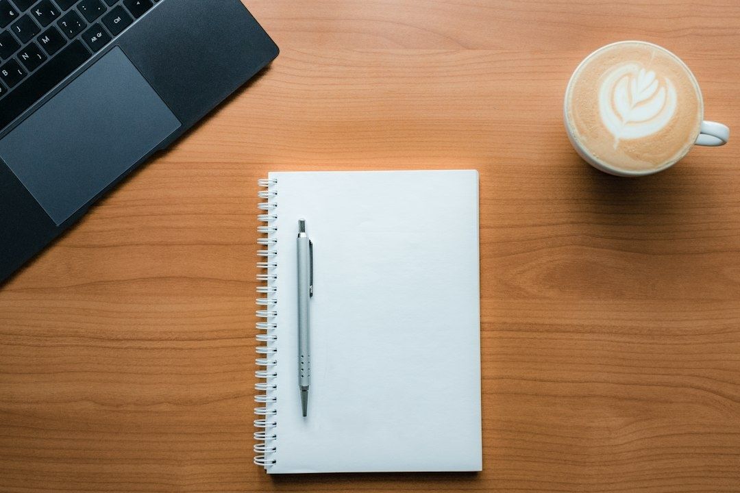 Anteckningsbok med penna bredvid laptop och kaffe på skrivbord
