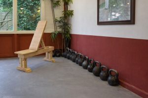 En träningsbänk i trä och en rad kettlebells längs en vägg.