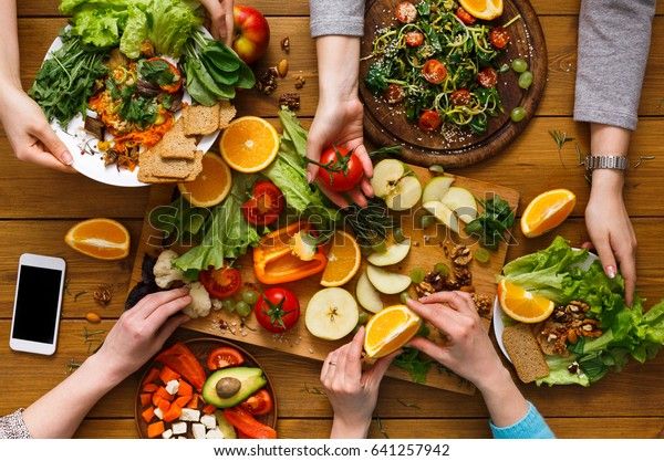 Händer runt ett träbord fyllt med färska grönsaker, frukter och glutenfria tillbehör.